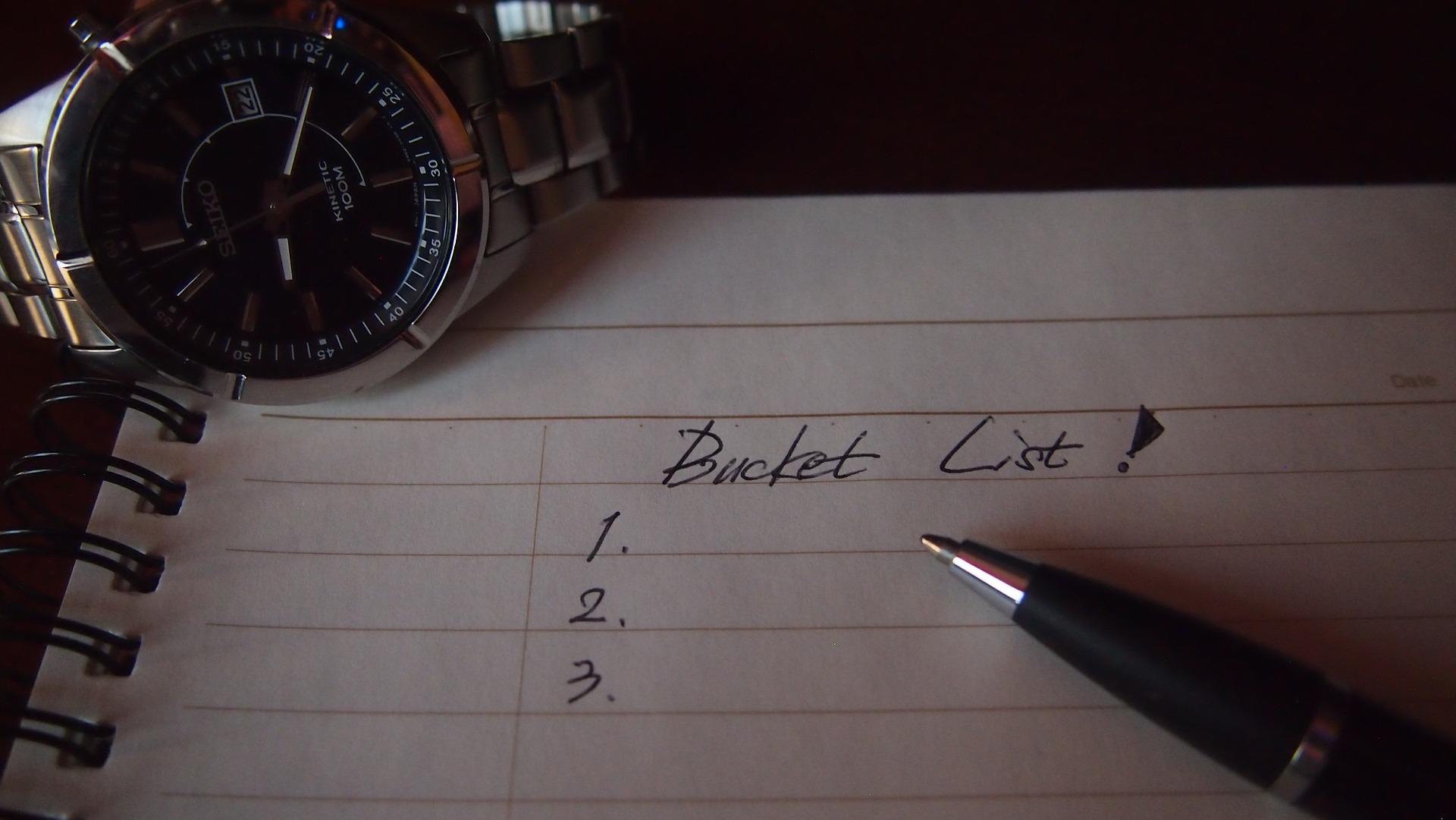 Notebook , pen and watch with a Bucket List written on the notebook.