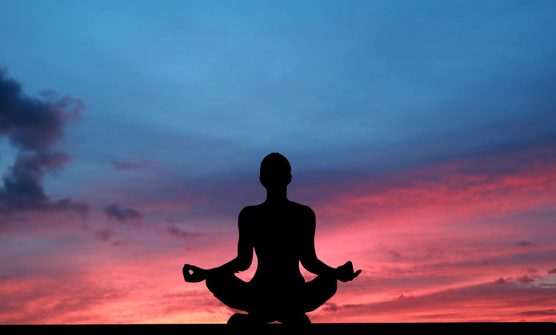 Silhouette of person meditating during a sunrise.